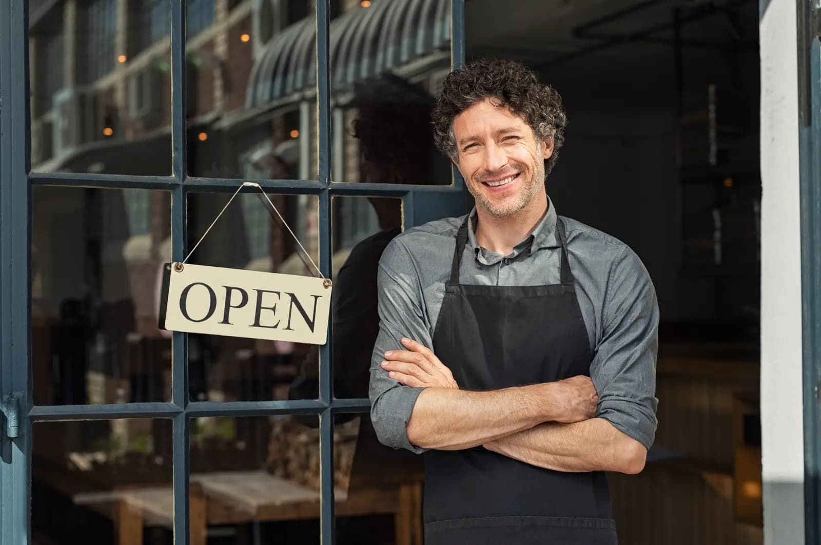 Propietario de restaurante sonriente frente al local con letrero abierto.