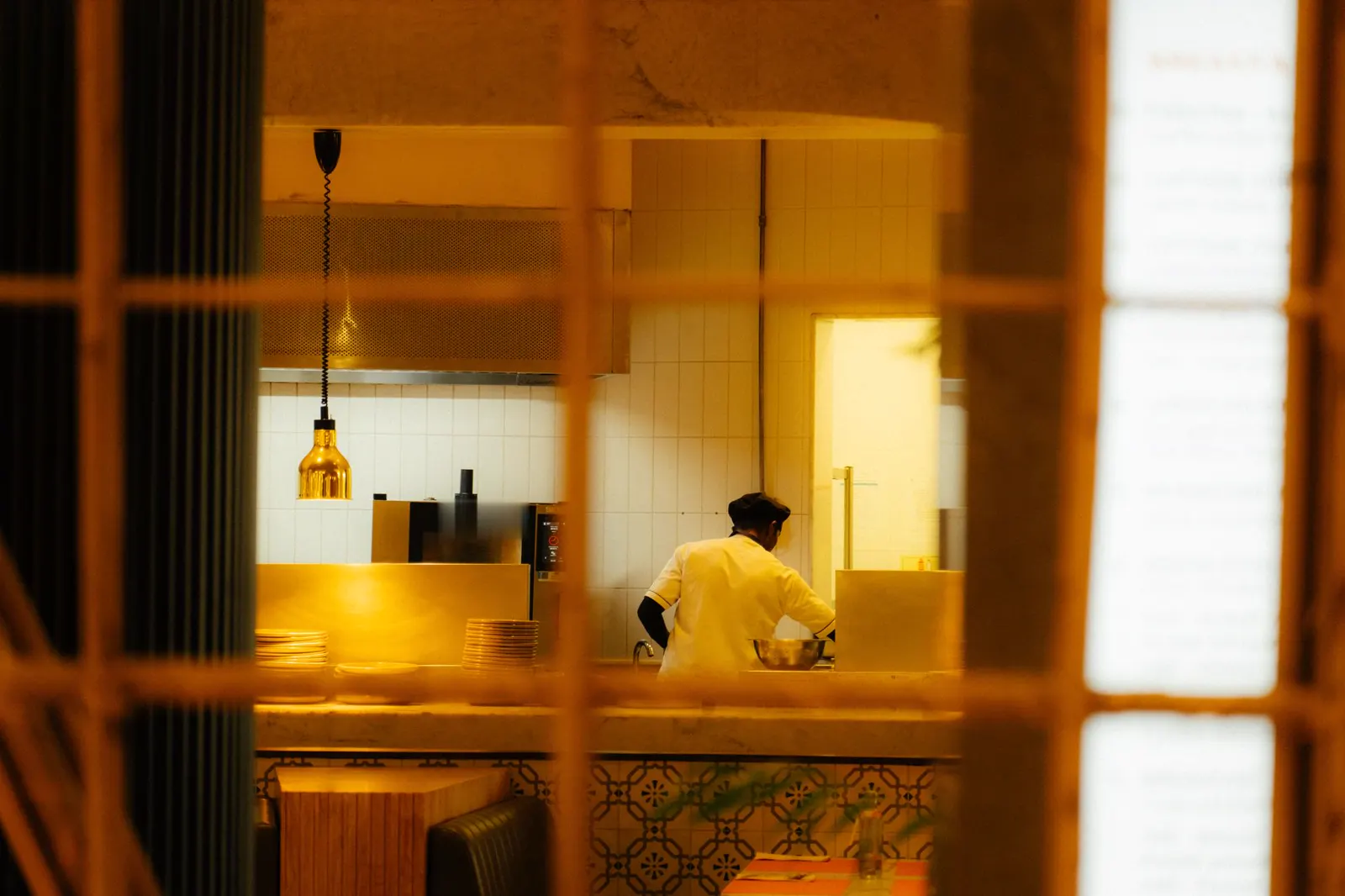 Cook working in a warmly lit restaurant kitchen at night, seen through the pass.